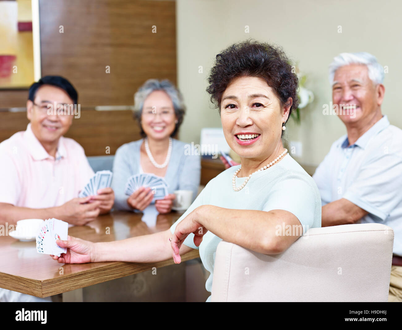 senior asian woman looking at camera smiling while playing cards with friends Stock Photo