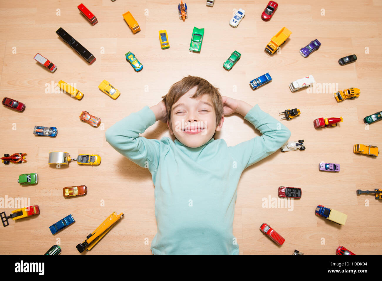 Adorable boy lying on the ground and dreaming with toy cars around