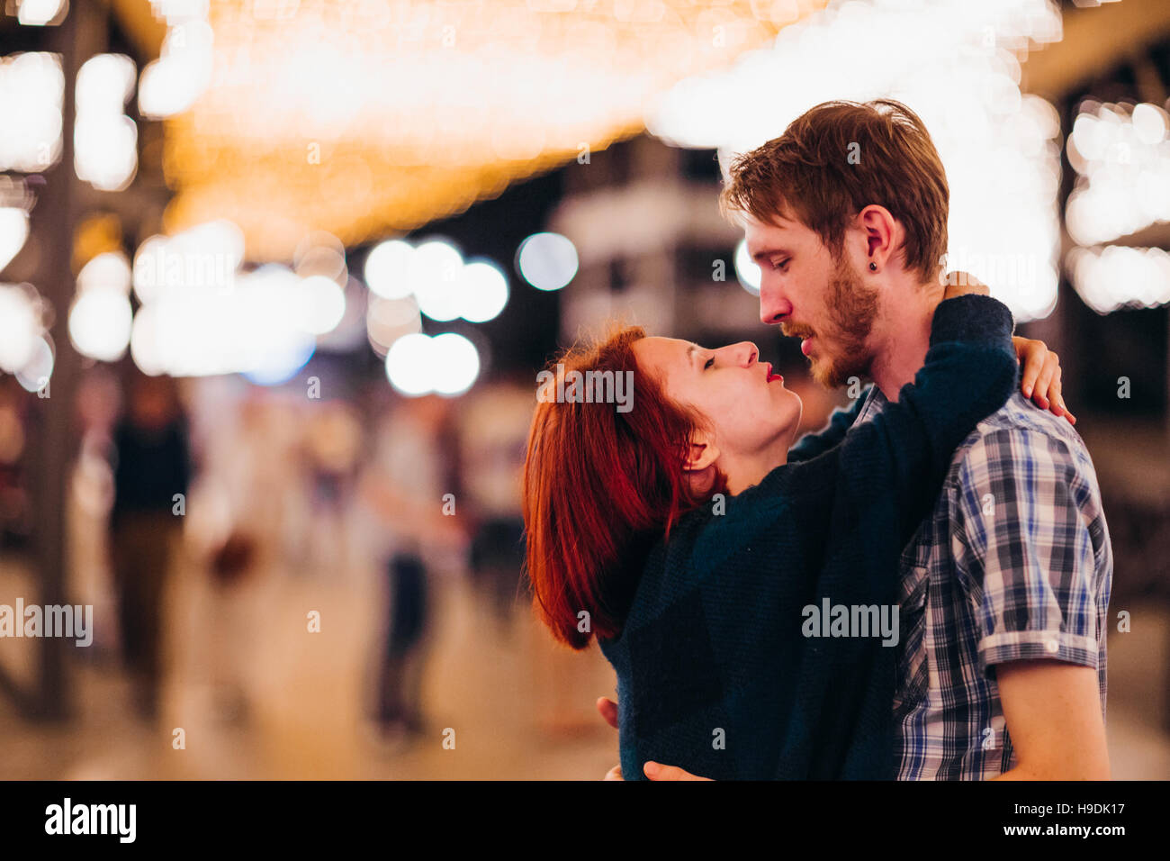 Happy couple embracing and kissing in the evening on a light garlands ...