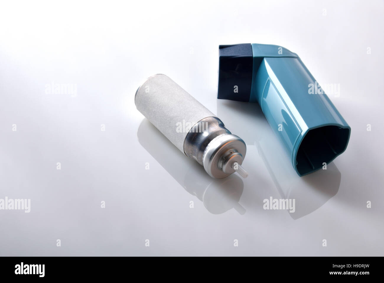 Cartridge and blue medicine inhaler on white glass table. Elevated view