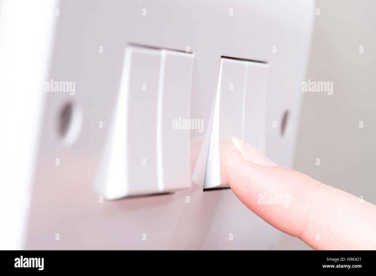 A manicured finger about to swithc on a light by pressing a switch on a white 4 gang light switch Stock Photo
