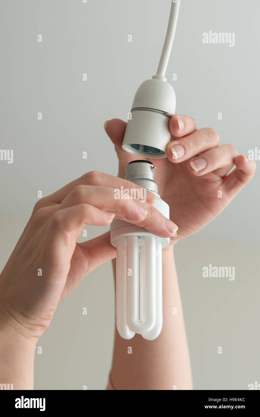 Hands fit or remove an energy saving light bulb from a hanging ceiling