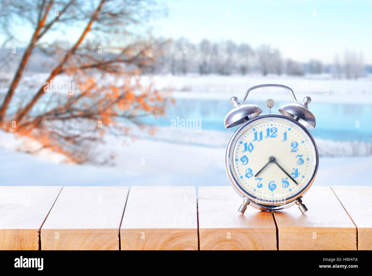 Vintage alarm clock on wooden table or bench on winter season background. Return to winter time. Fall back time. Daylight savings end Stock Photo