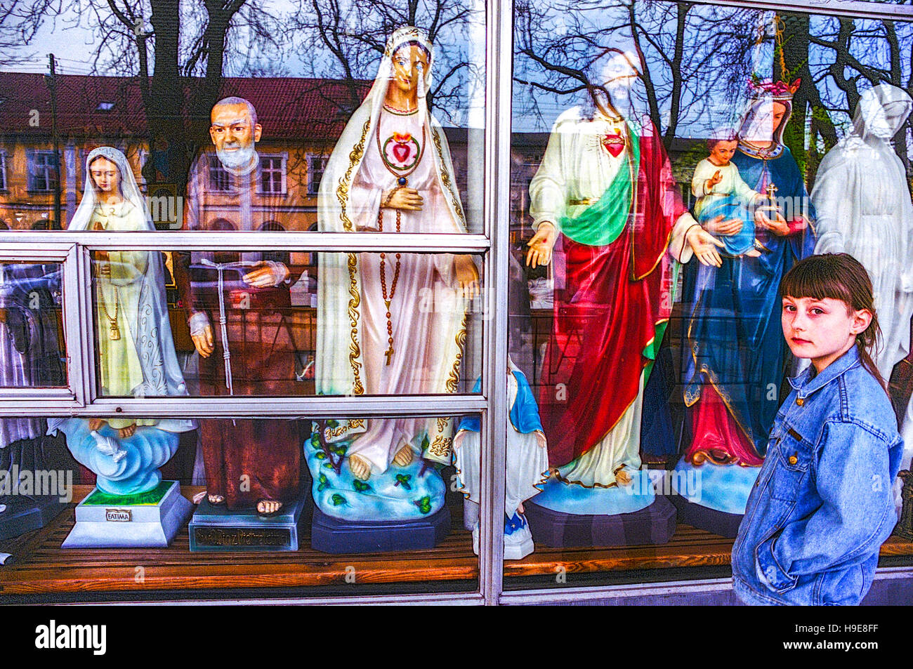 Czestochowa Poland, Young Preteen Girl in front of Shop Window Display with Religious Votive Products Articles Sacred Roman Catholic Saints Stock Photo