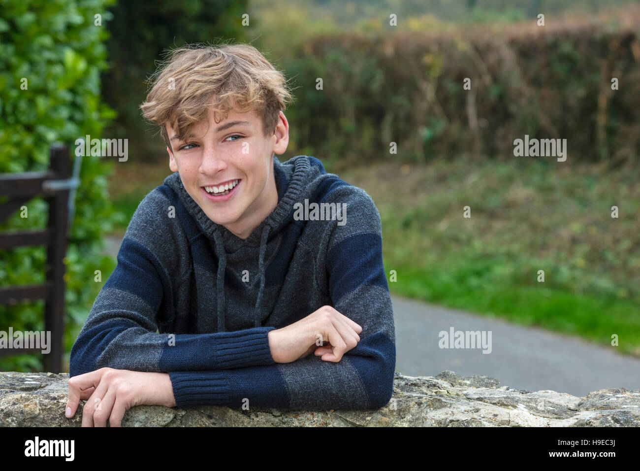 Young happy laughing smiling teenager male boy blond child outside leaning on a wall in autumn fall sunshine Stock Photo