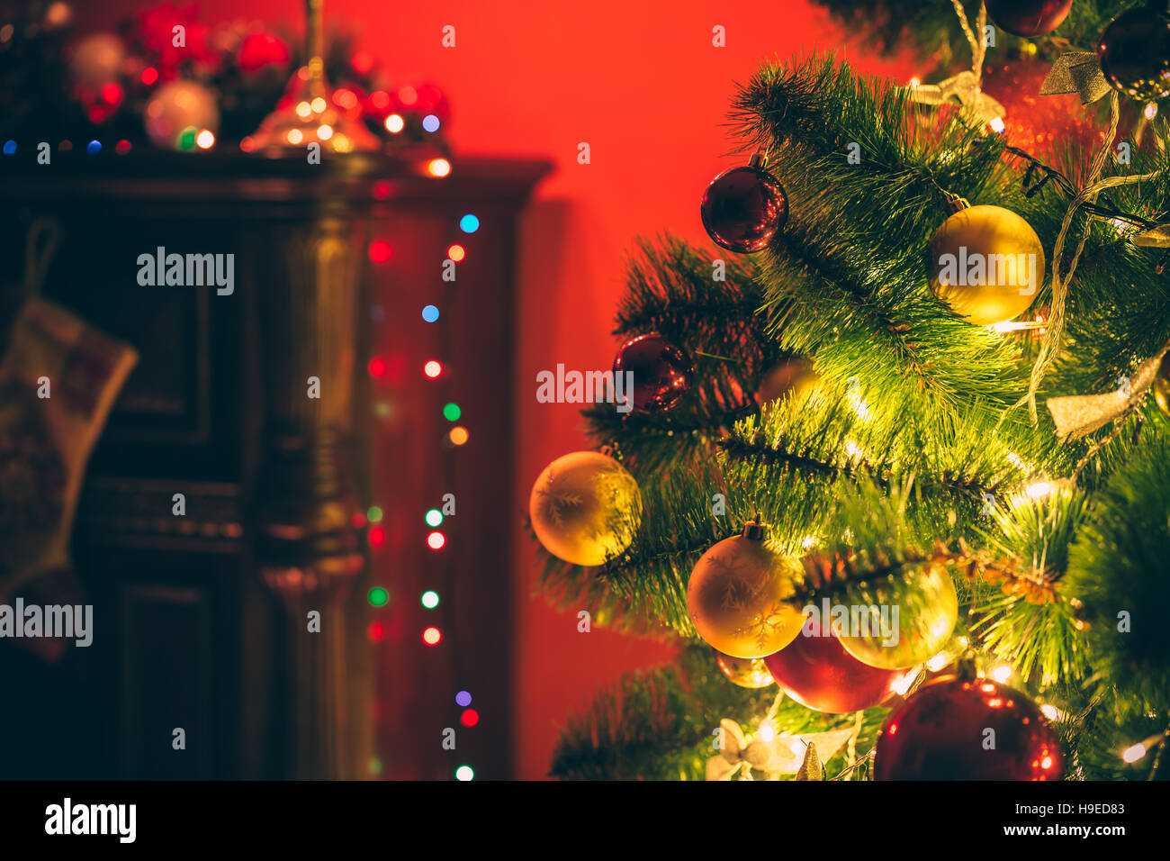 Beautiful decorated Christmas tree with red and goldish baubles and garland, in the new-year background with fireplace and socks. The idea for postcar Stock Photo