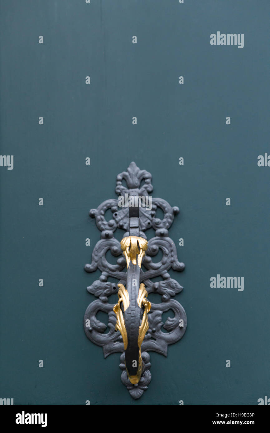 A dark green painted wooden door of a villa with elegant metal ornaments, golden knobs and knocker. Detail view of a knocker. Stock Photo