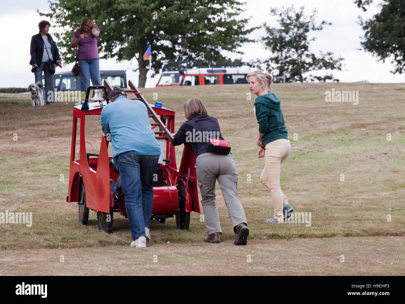 A man and a woman push a novelty fire engine soapbox racer back uphill Stock Photo