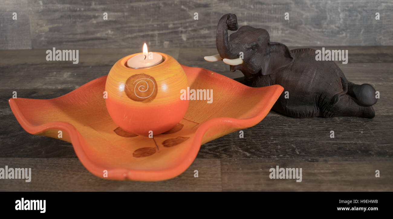 A decorative Bowl with a burning candle on a surface of wood, decorated with a figure of the elephant. Stock Photo