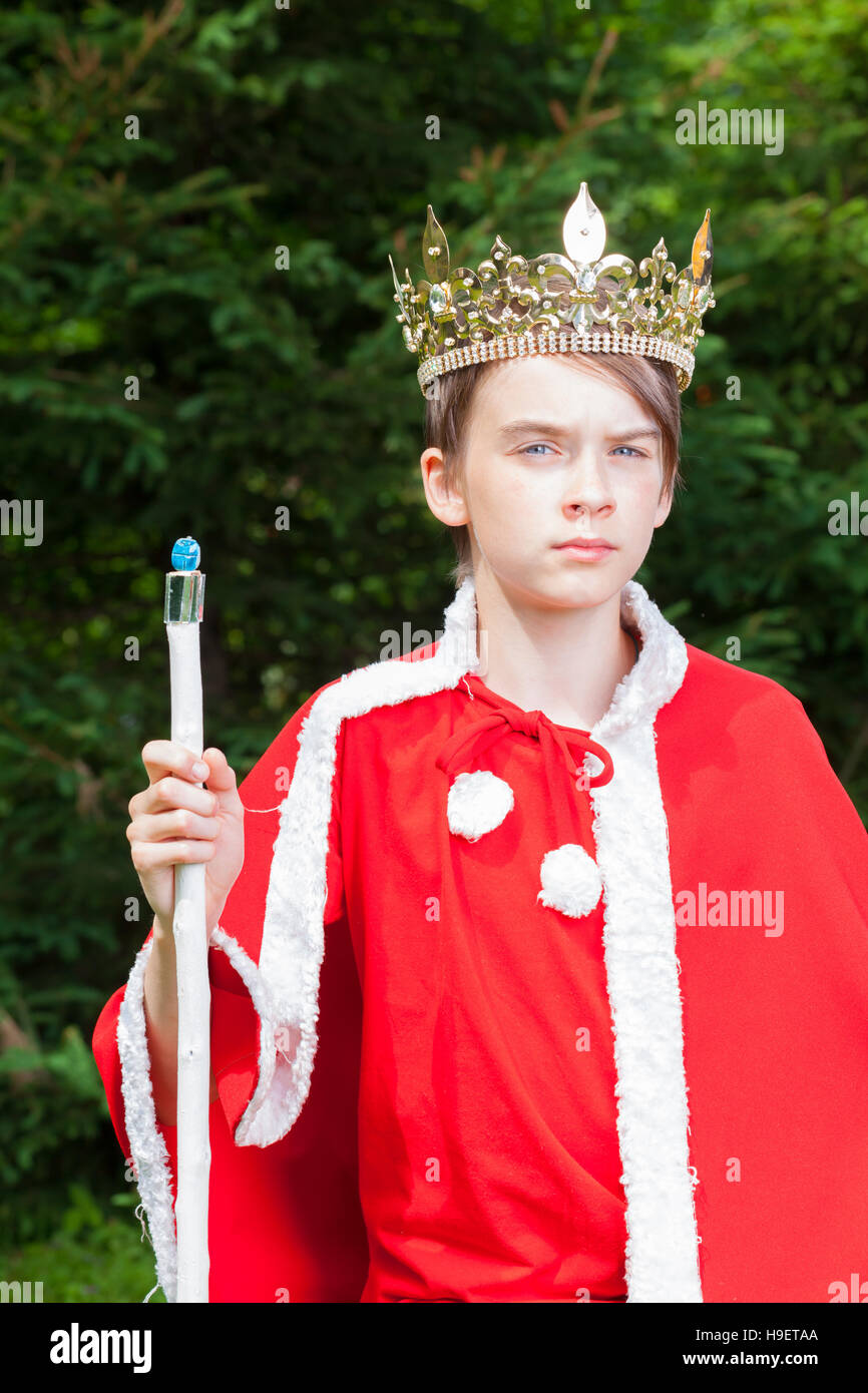 Cute teen boy wearing crown and red costume holding a scepter pretending to be a king Stock Photo