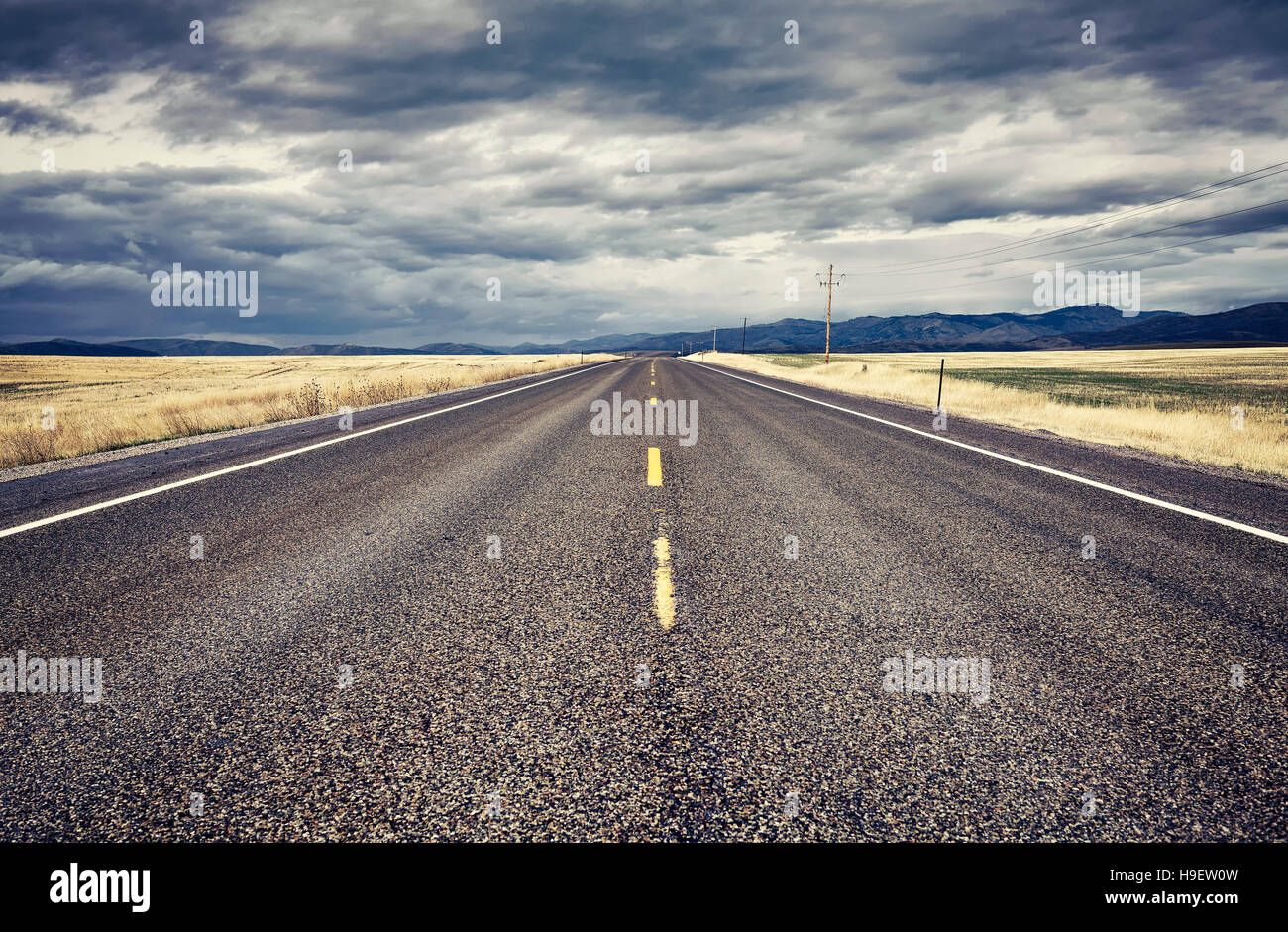 Retro stylized empty rural road with rainy clouds, USA. Stock Photo