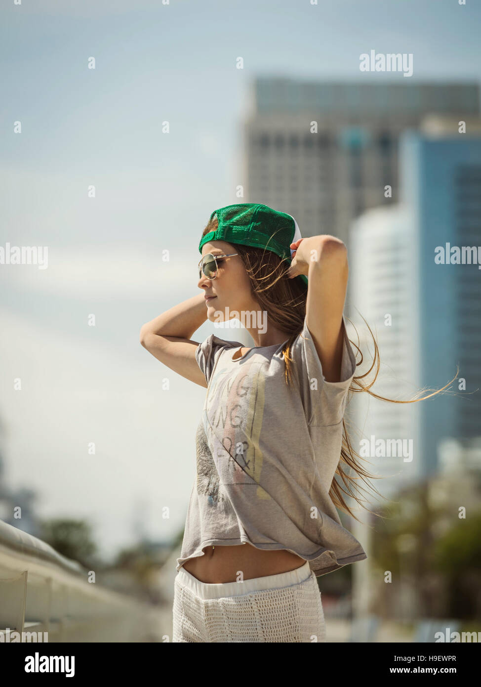 Caucasian woman wearing baseball cap and sunglasses in wind Stock Photo