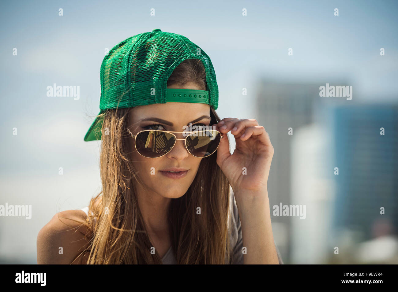 Caucasian woman wearing baseball cap peering over sunglasses Stock Photo