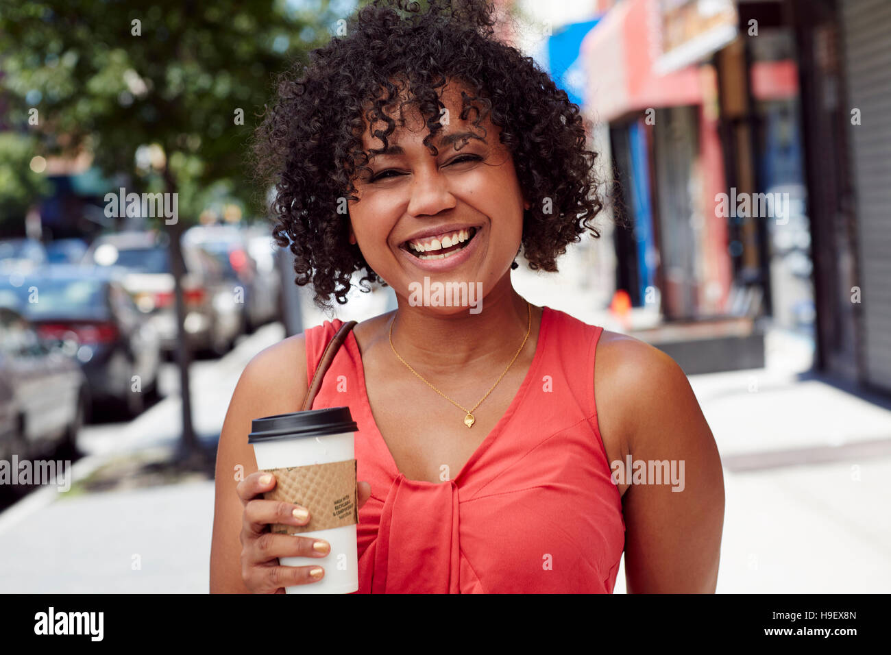 Smiling woman carrying coffee on city sidewalk Stock Photo
