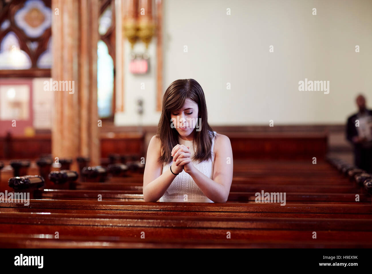 Kneeling Caucasian woman praying in church pew Stock Photo