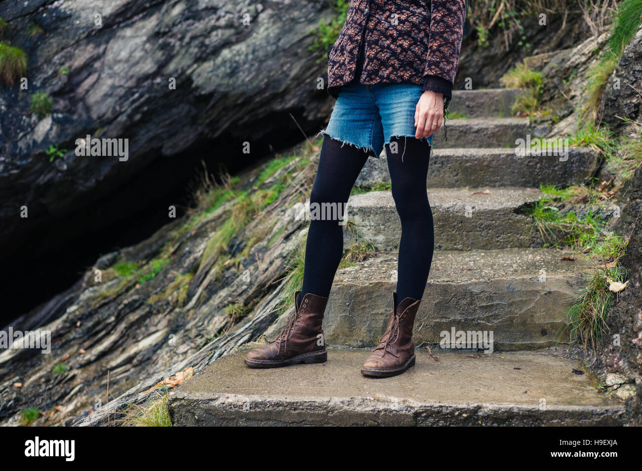 A young woman wearing hiking boots is standing on some concrete steps