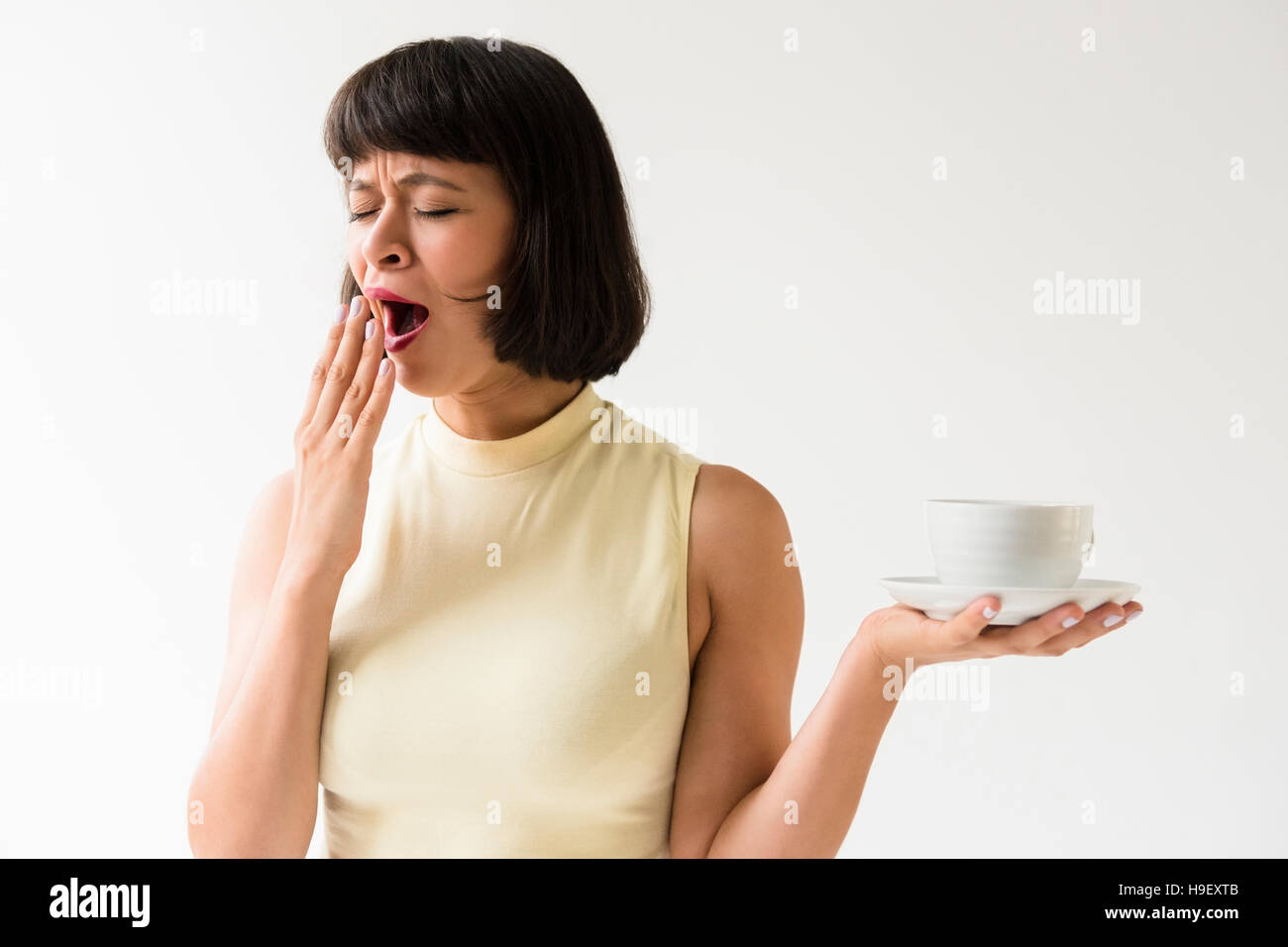 Yawning Hispanic woman holding coffee cup Stock Photo