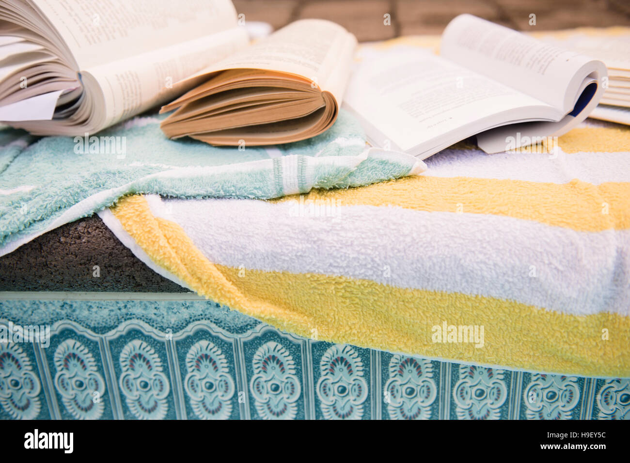 Books and towels at the edge of swimming pool Stock Photo