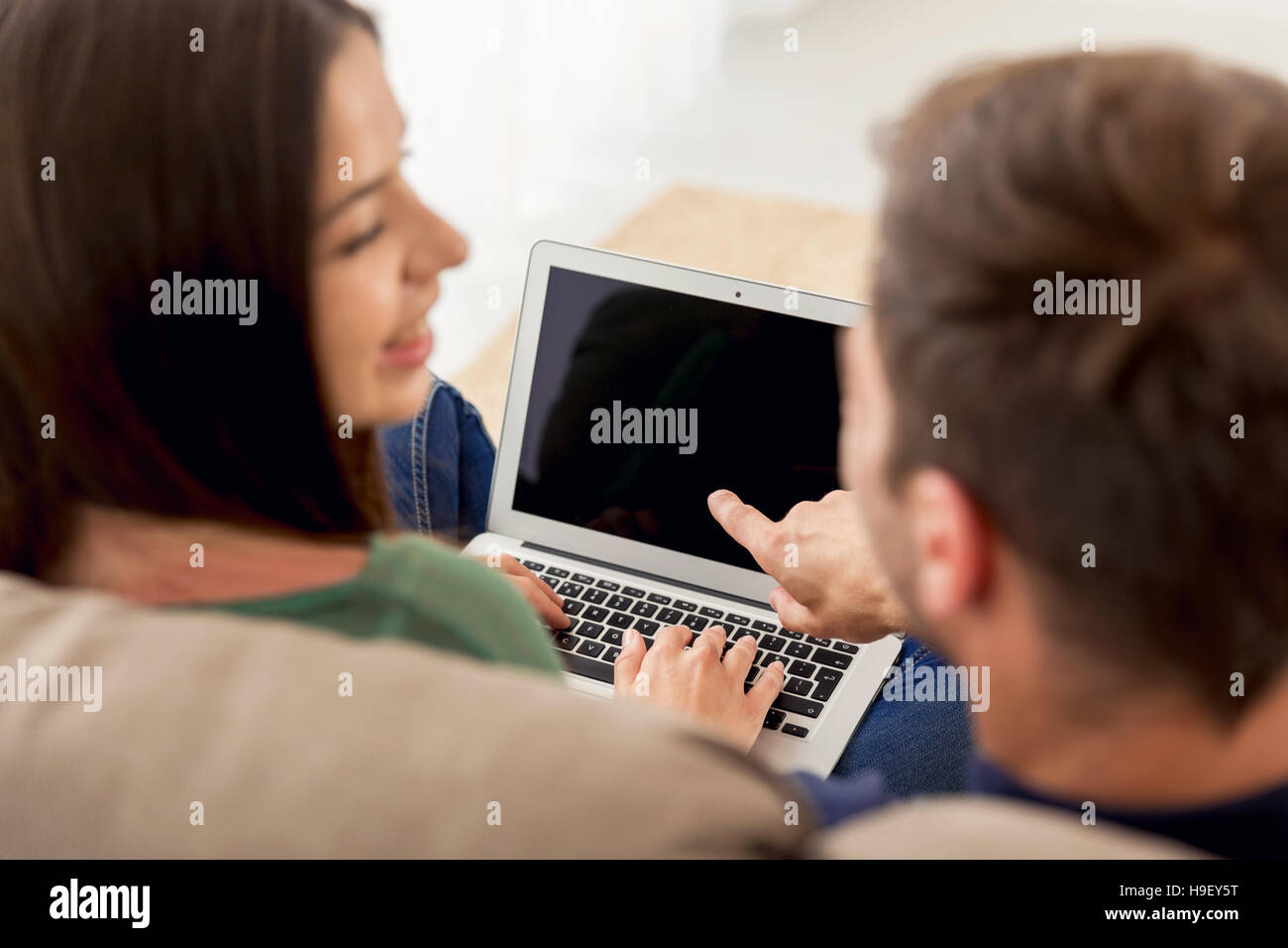 Young couple sitting on the sofa and watching something on a laptop ...