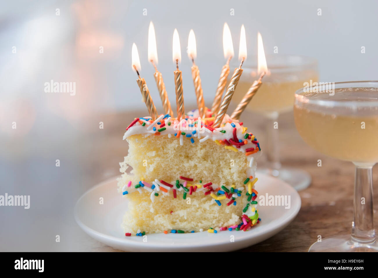 Candles burning on slice of cake with sprinkles near champagne Stock Photo