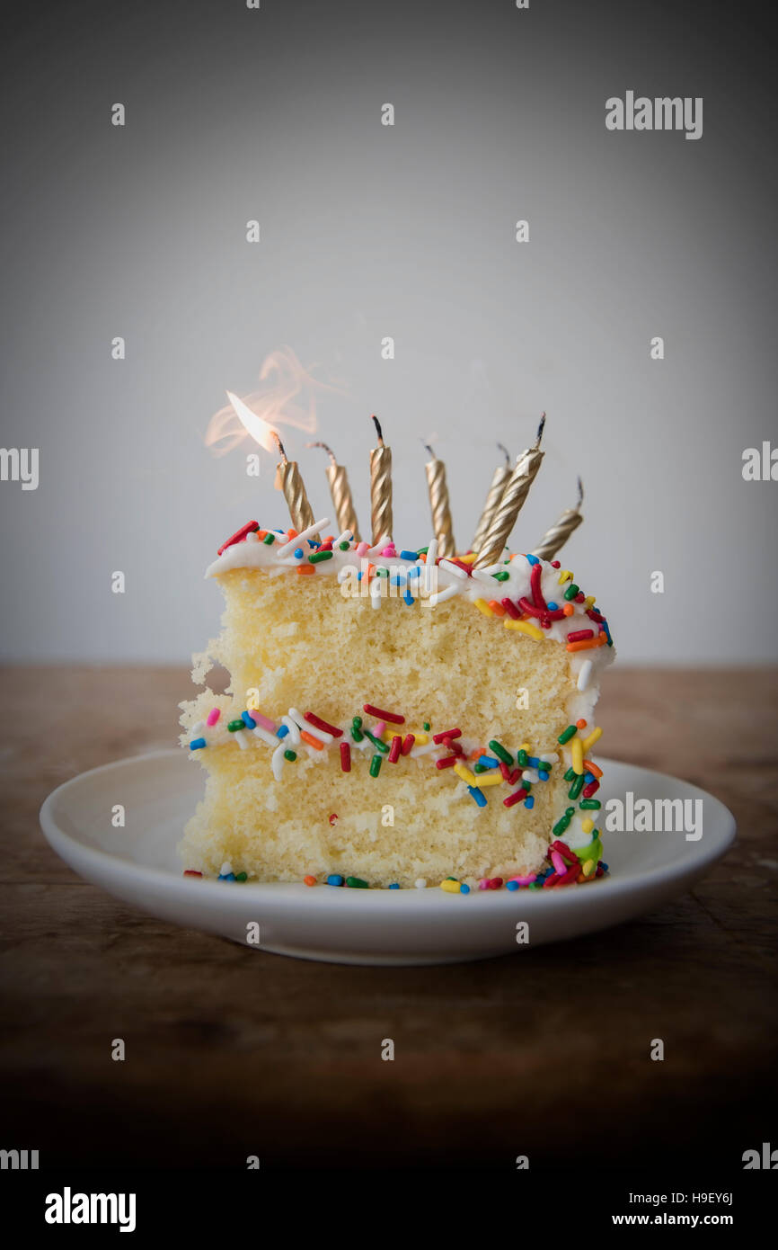 Flickering candle burning cake with sprinkles on plate Stock Photo