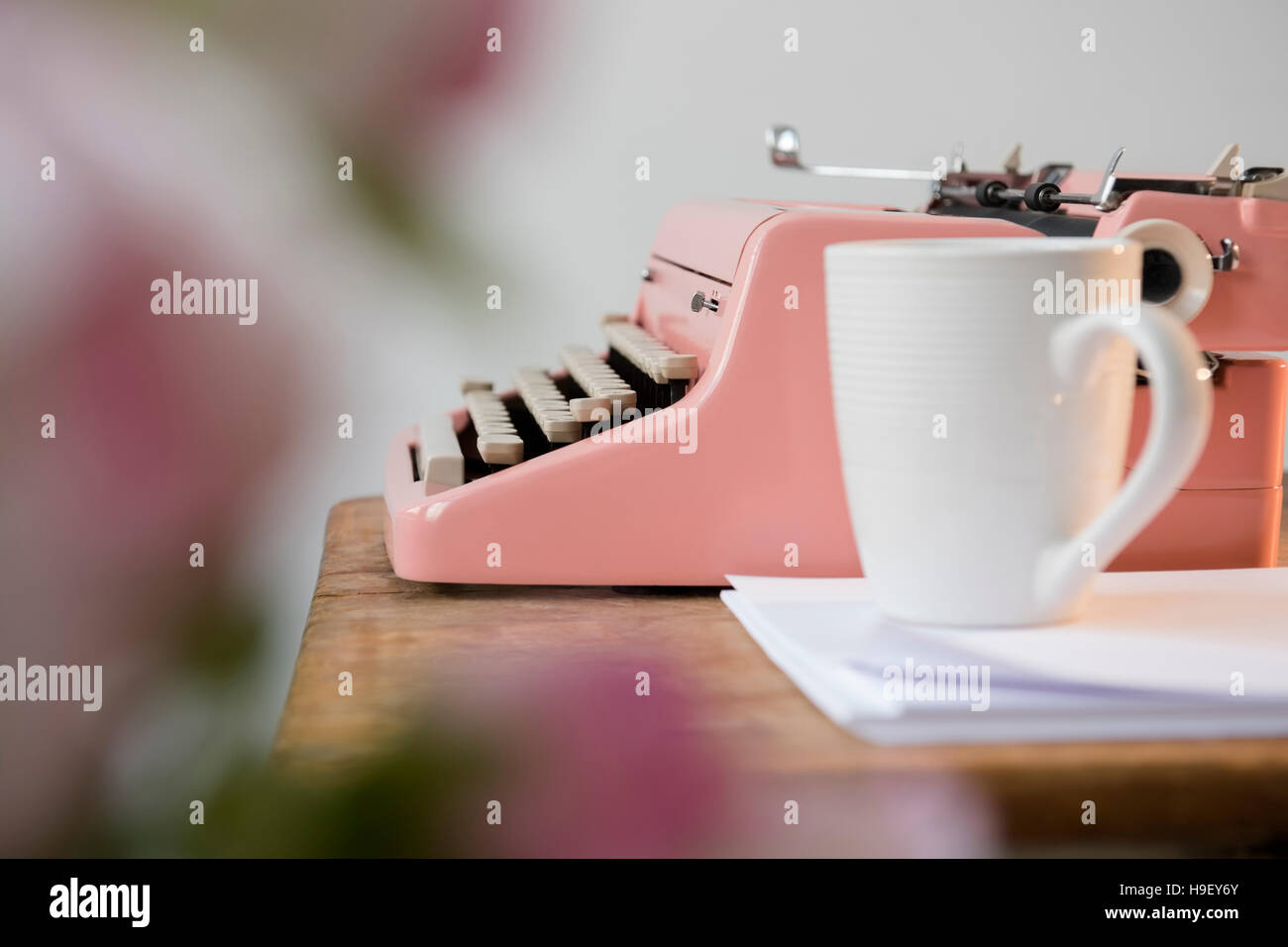 Coffee cup on pile of paper near pink typewriter Stock Photo