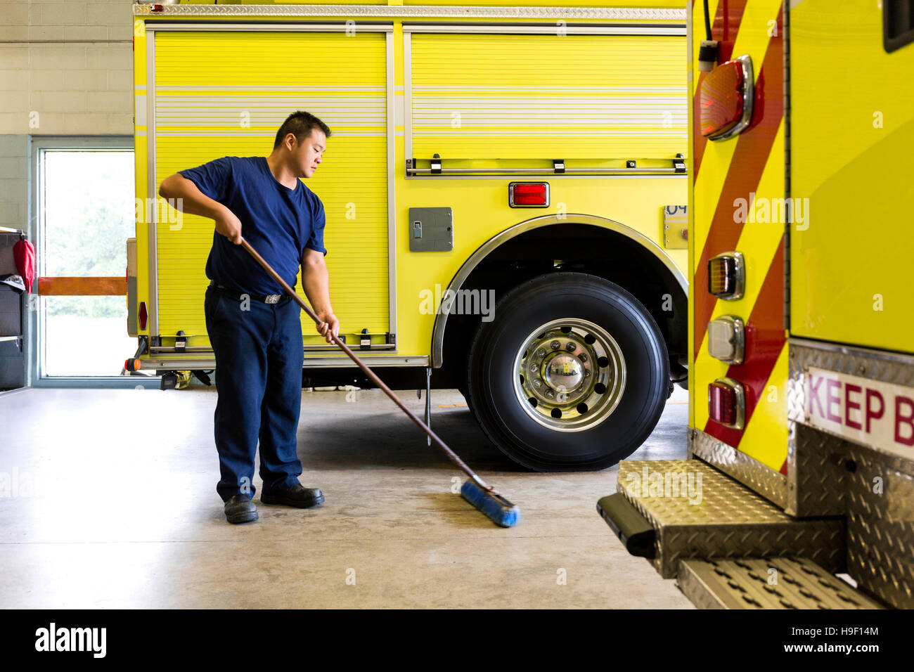 Chinese fireman sweeping floor near fire trucks Stock Photo