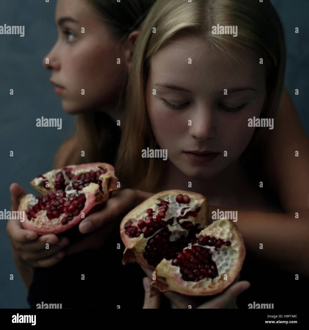 Intertwined Caucasian girls holding sliced pomegranate Stock Photo