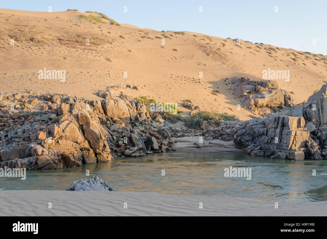 Kunene River in front of towering ancient Namib Desert sand dunes of Namibia and Angola Stock Photo