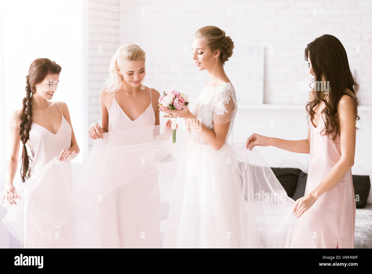 Amused bridesmaids touching the dress of the bride Stock Photo