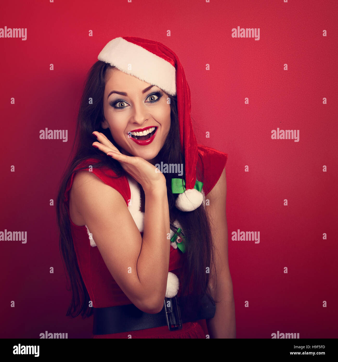 Beautiful surprising woman with open mouth in Santa Claus Christmas costume looking on bright red background with empty copy space. Closeup portrait Stock Photo