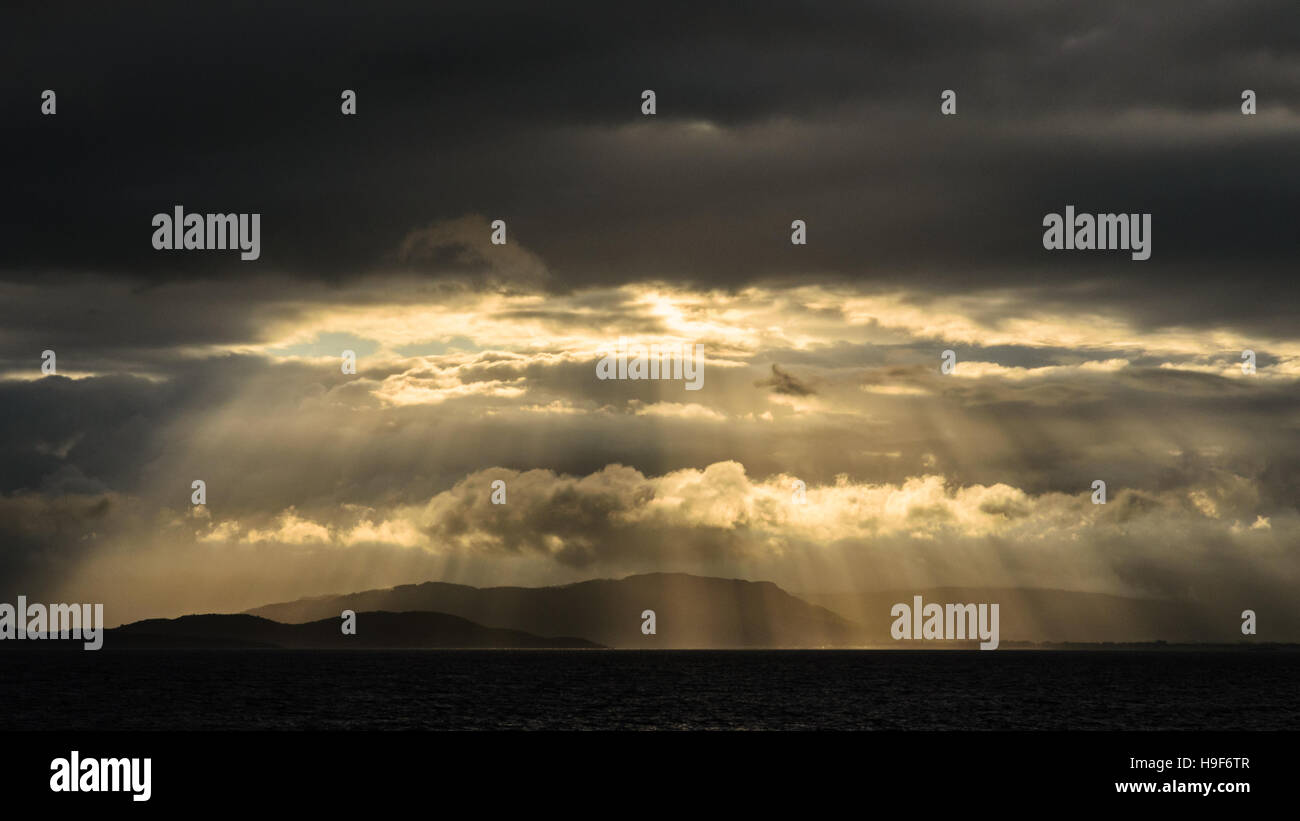 Beautiful sun rays through the clouds over the sea near Isle of Mull and the mainland of Scotland. Image was taken from the ferry from Craignure to Oban. Stock Photo