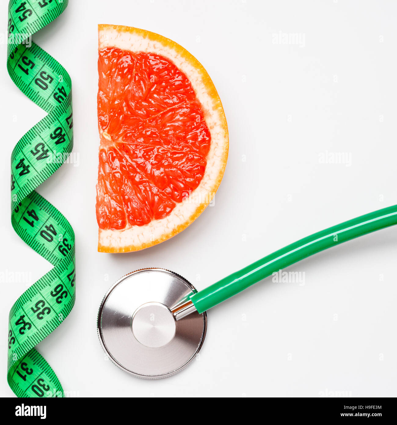 Diet healthy eating weight control concept. Grapefruit with measuring tape and stethoscope on white scales Stock Photo