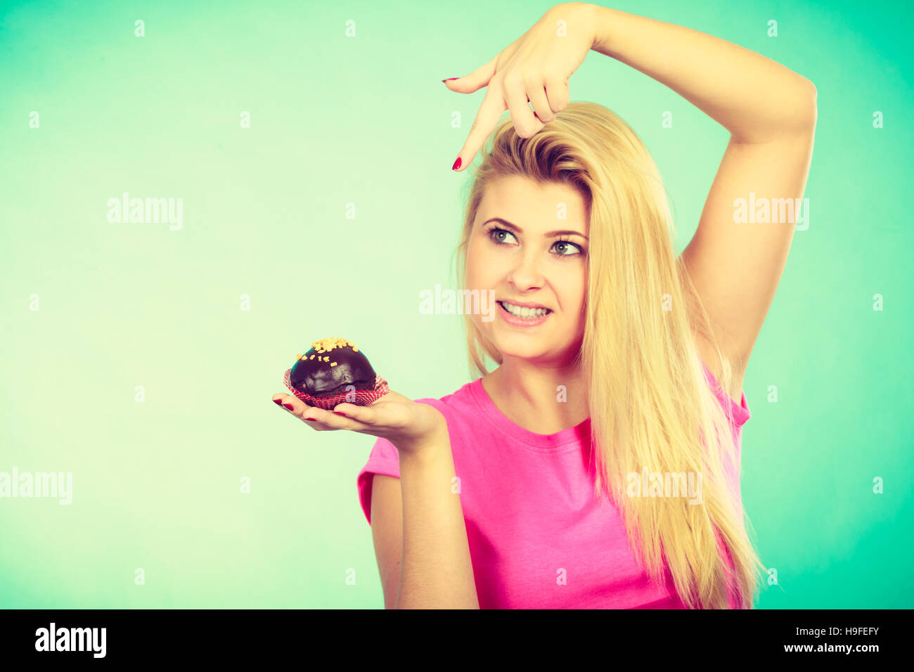 Diet, sweets, food concept. Cute blonde attractive woman about to eat delicious chocolate cupcake Stock Photo