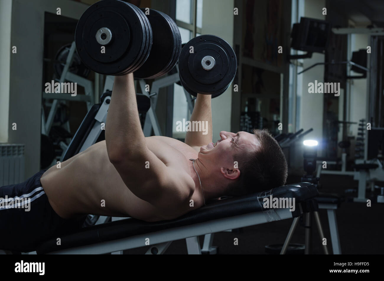Young muscular man performs a dumbbell chest press on an incline bench at the gym Stock Photo