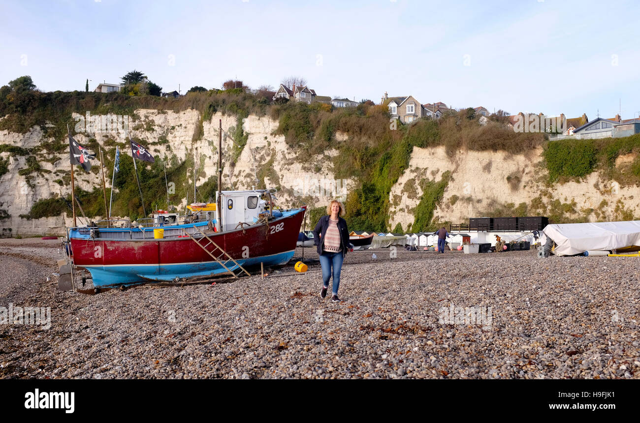 Woman walking by Fishing boats on the beach at Beer Devon West Country UK Stock Photo