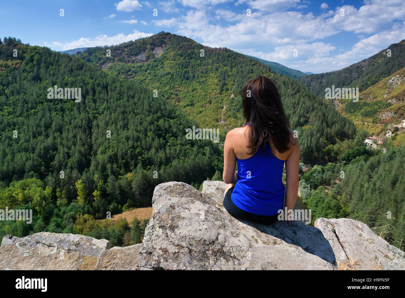 A girl is sitting on the edge of a cliff and looking at a mountain ...