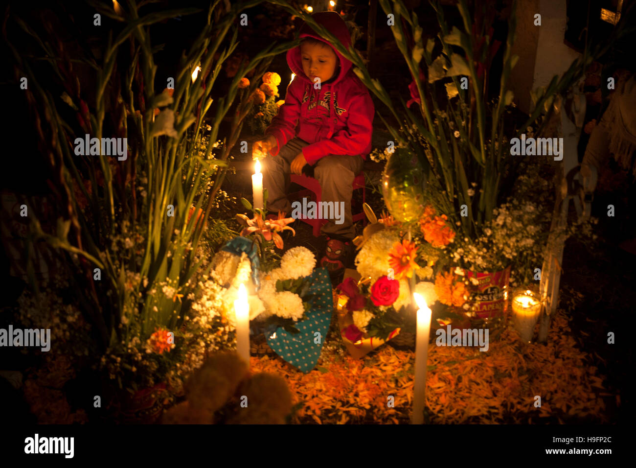 A boy sits in a tomb decorated with candles and yellow marigold flowers during Day of the Dead celebrations in Mexico City Stock Photo