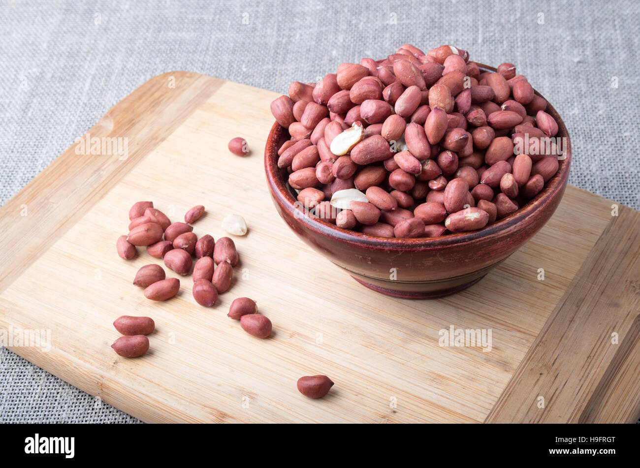 Old bowl filled with raw peanuts on a wooden stand on a fabric background Stock Photo