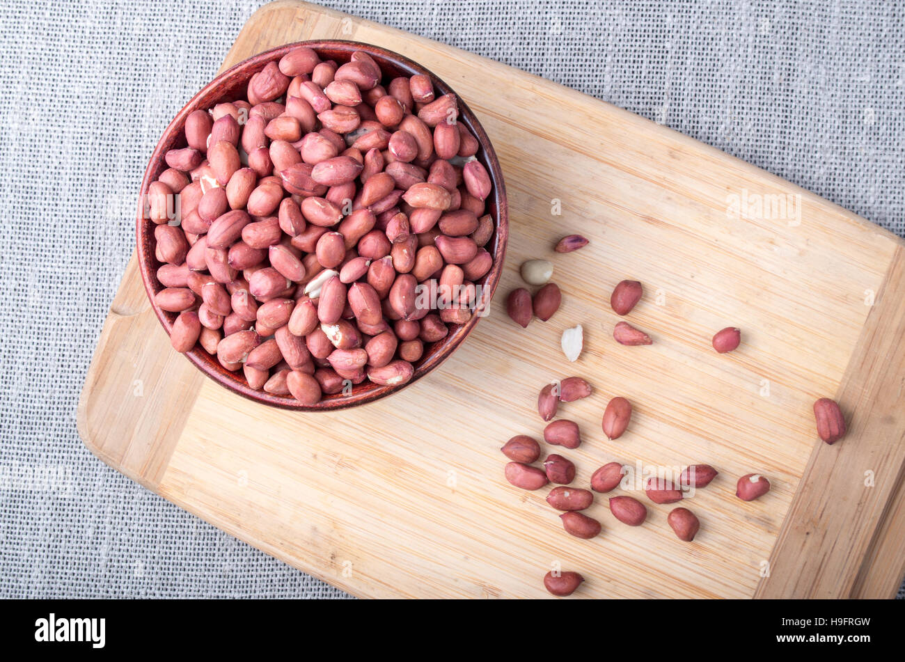 Top view of a brown bowl with raw peanuts on a wooden board on a background of gray tablecloth Stock Photo