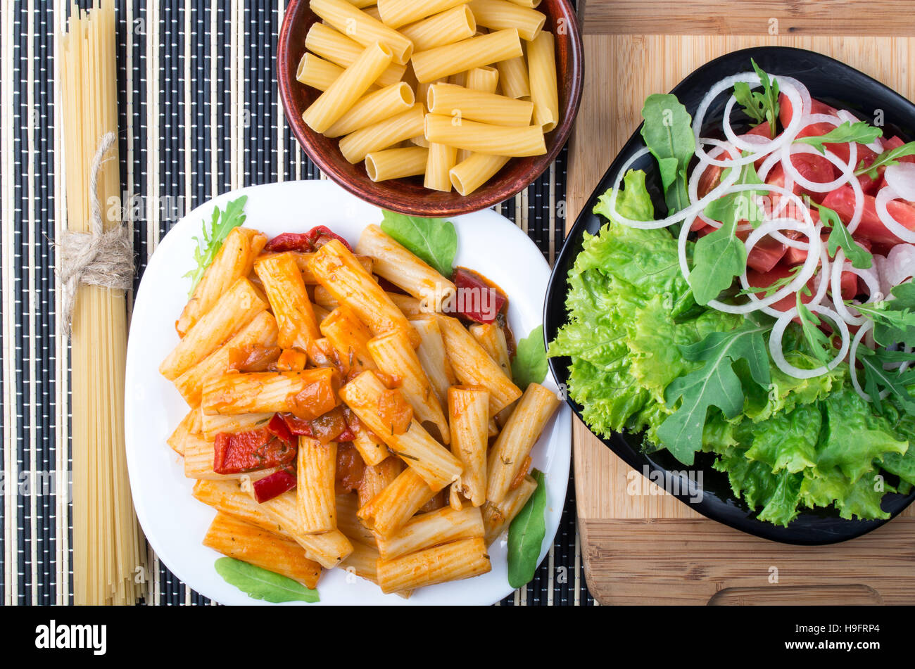 Top view of cooked rigatoni pasta with vegetable sauce and a plate of fresh vegetable salad
