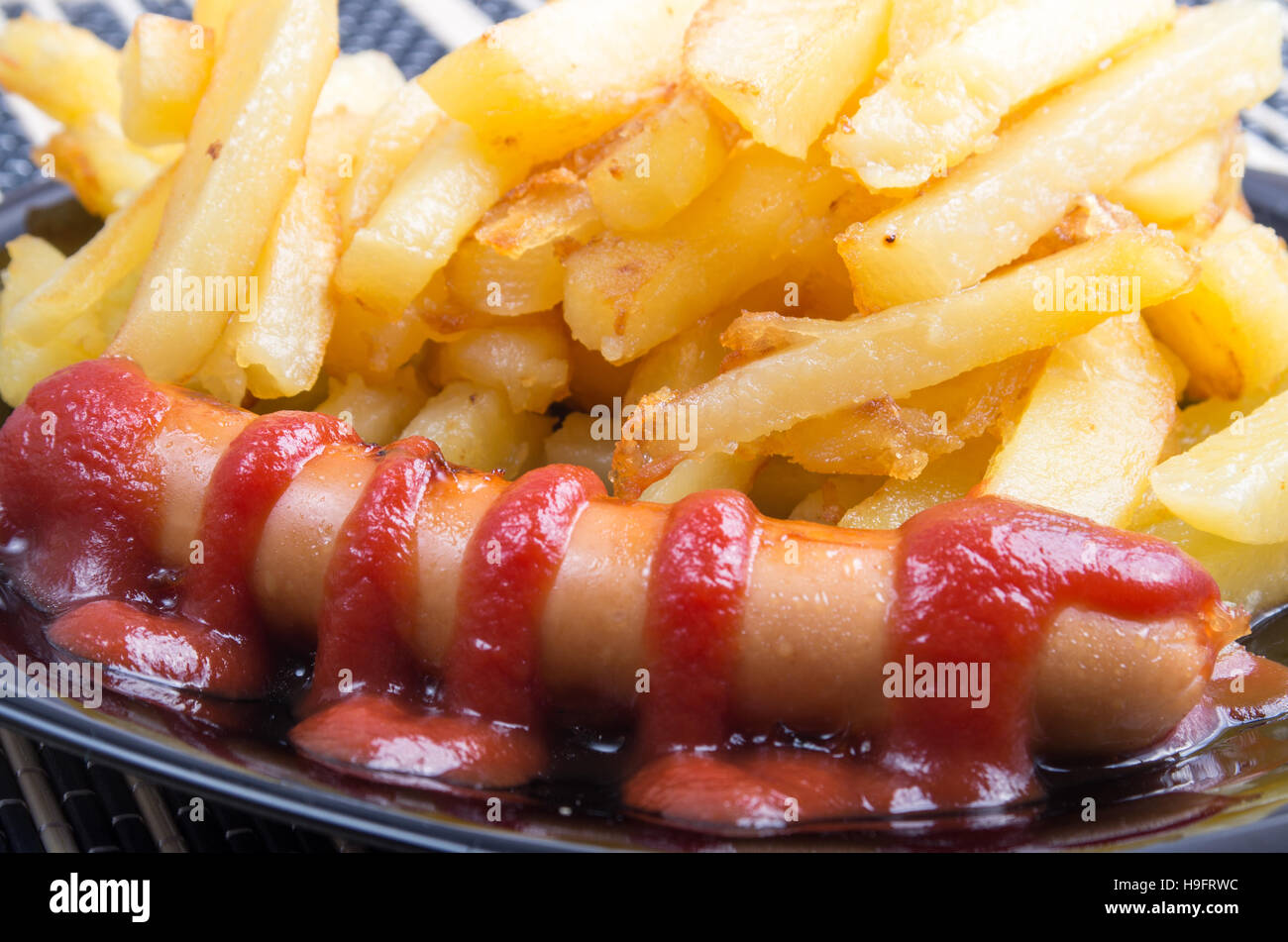 Hot fried sausage decorated with tomato ketchup on a plate next to the fries closeup Stock Photo