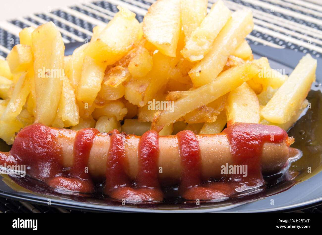 Fried sausage and french fries decorated with tomato sauce on a plate