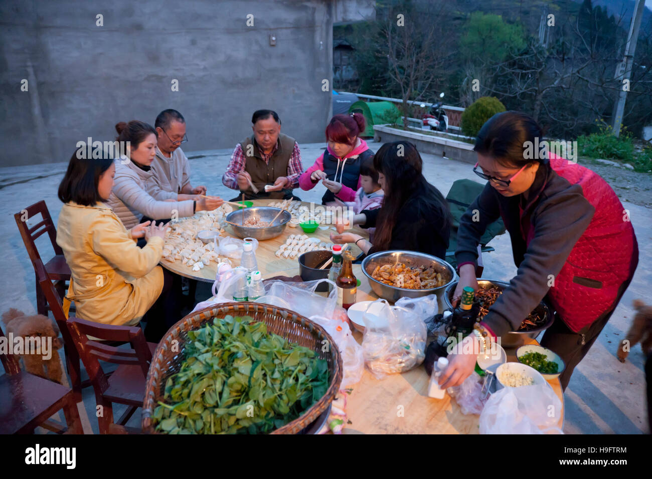 A group of friends make fresh dumplings for dinner during a farm-stay holiday in the mountains of west China. Stock Photo