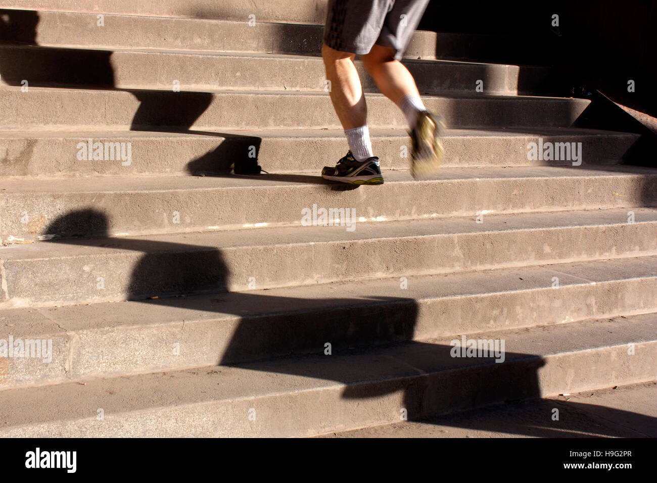 Legs of a man in sneakers and shorts running up the city stairs and long shadows. Motion blur Stock Photo