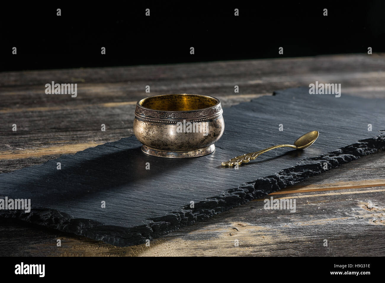 Ancient melkhiorovy saltcellar with spoon on a black slate plate in style  rustic Stock Photo