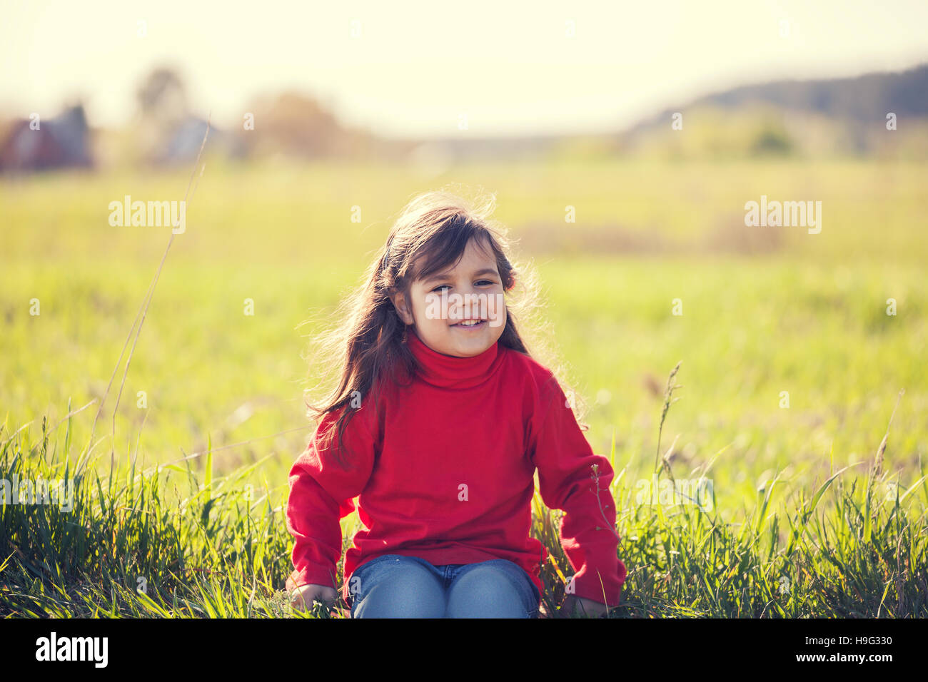 Happy smiling little girl sitting on the field in sunny day Stock Photo ...