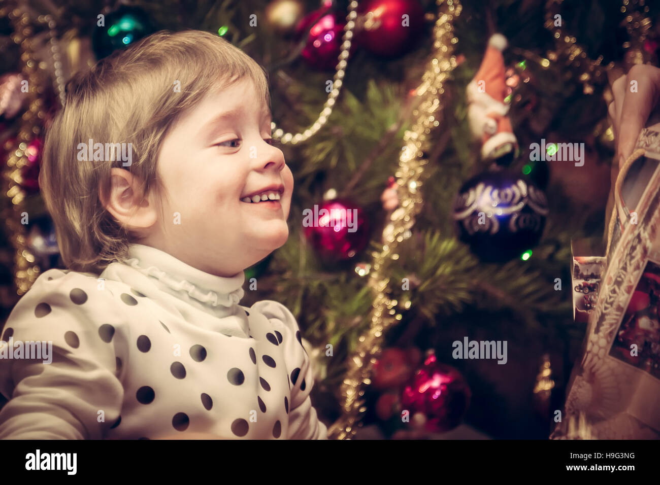 Happy smiling child getting Christmas gift with Christmas tree on background in retro style Stock Photo