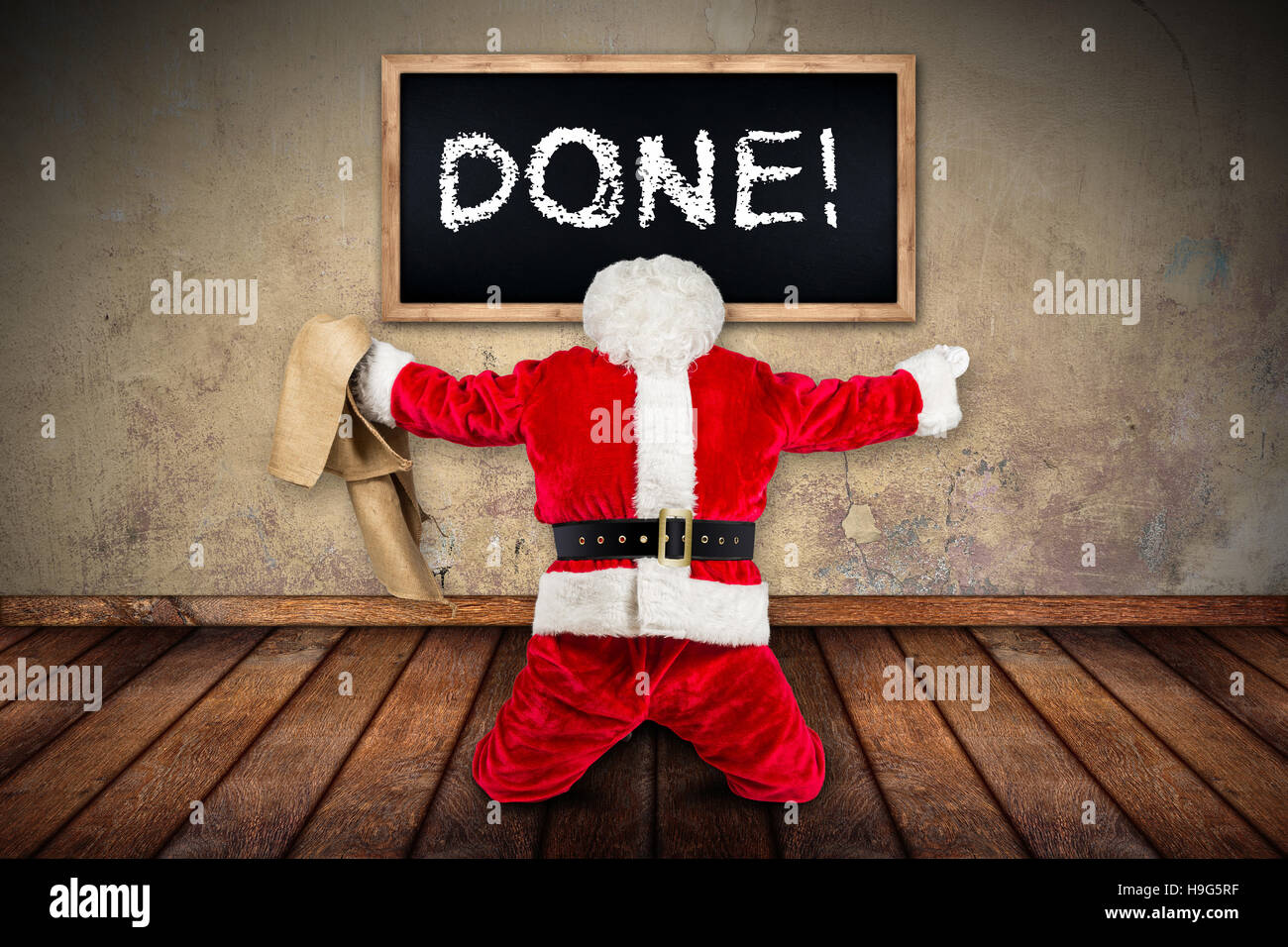 funny crazy hilarious red white santa claus celebration clench fist holding bag in the air job done blackboard on wooden floor interior room Stock Photo