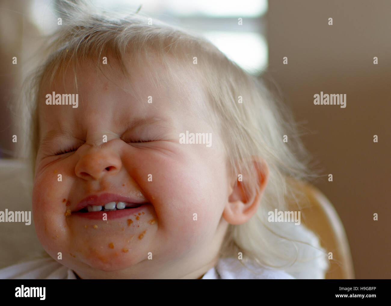 Blond baby girl, giggling and laughing with chocolate on face squinting eyes Stock Photo